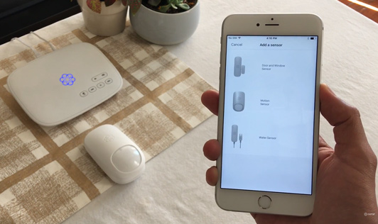 Man looking at smartphone display showing a home security system motion sensors products.