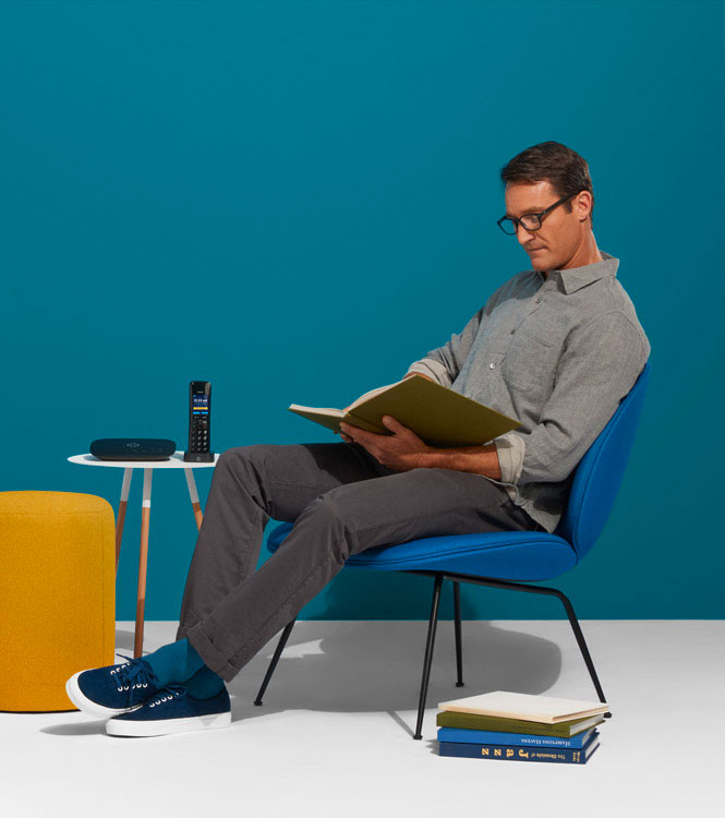 Ooma Home Phone Service Hero Image - A man sitting down with Telo Home Phone on a table next to him