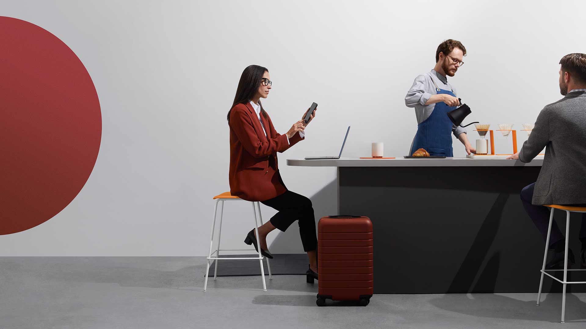 Woman with a phone and laptop at a counter with a barista and another customer