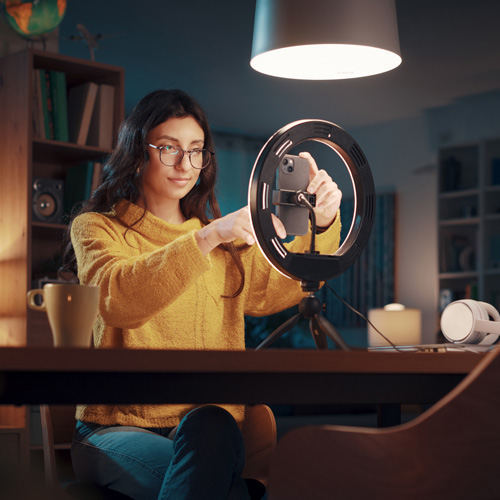 woman in her home office sitting at a desk with her smartphone in a ring light